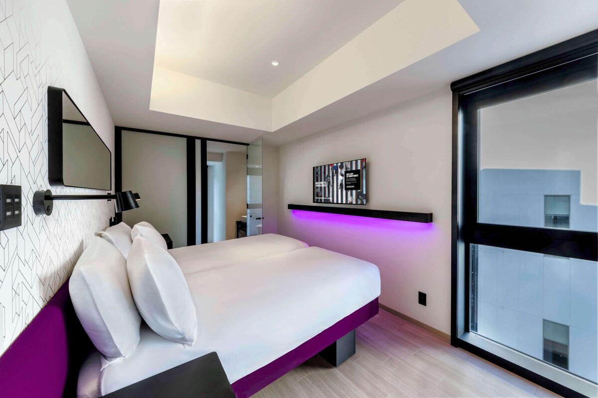 A modern bedroom with a bed, a large window, and a wall-mounted TV.