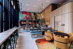A modern interior with a long wooden table, blue and yellow seating, and a colorful mural. - YOTEL Tokyo Ginza (Tokyo)