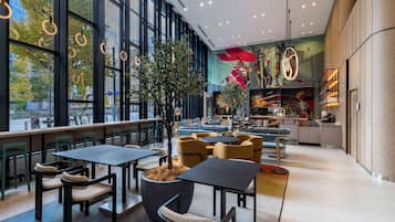 A modern cafe with large windows, tables, chairs, and a central plant.