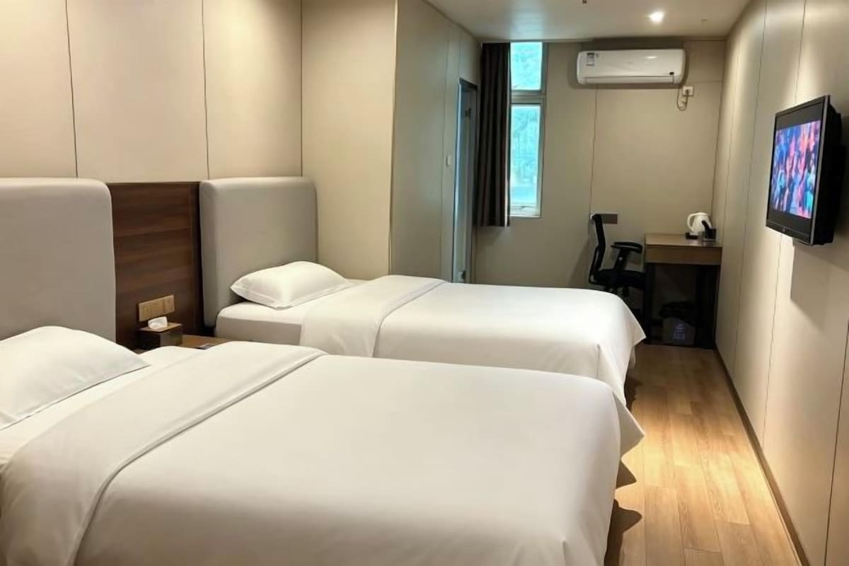 A hotel room with two beds, a desk, a chair, and a television.