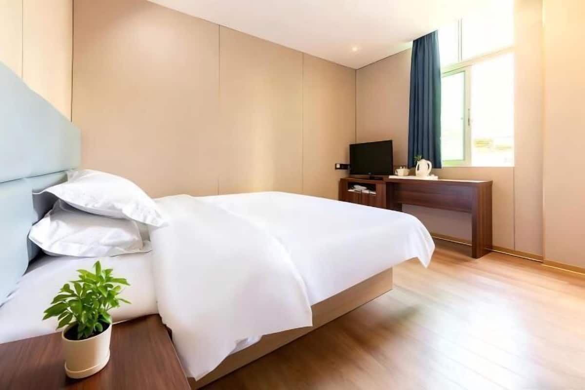 A hotel room with a bed, a TV, a desk, and a window.