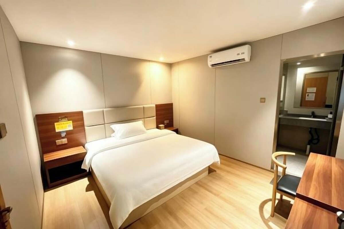 Quarto de hotel com cama, mesas de cabeceira, escrivaninha e espelho.