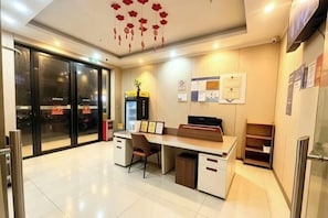 Uma área de recepção de hotel com balcão, cadeiras, lixeira e geladeira.