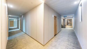 Un pasillo largo y estrecho con piso de madera y paredes blancas. Hay puertas a la derecha y un cartel sobre una de ellas.