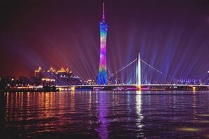 A nighttime view of a bridge with a tall tower, illuminated by colorful lights, reflecting on the water. - Baiyuan Hotel (Baogang Avenue Subway Station) (Guangzhou)