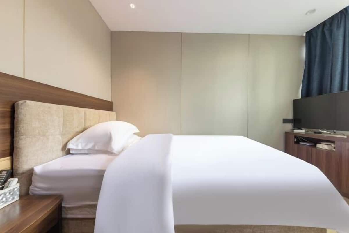 A hotel room with a bed, a nightstand, a TV, and a wooden headboard.