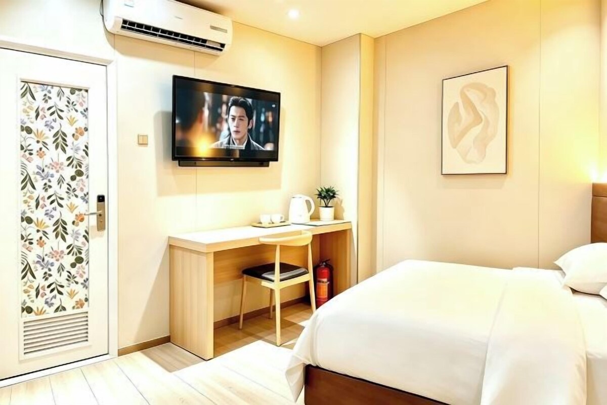 Quarto de hotel com cama, escrivaninha, cadeira, televisão e extintor de incêndio.