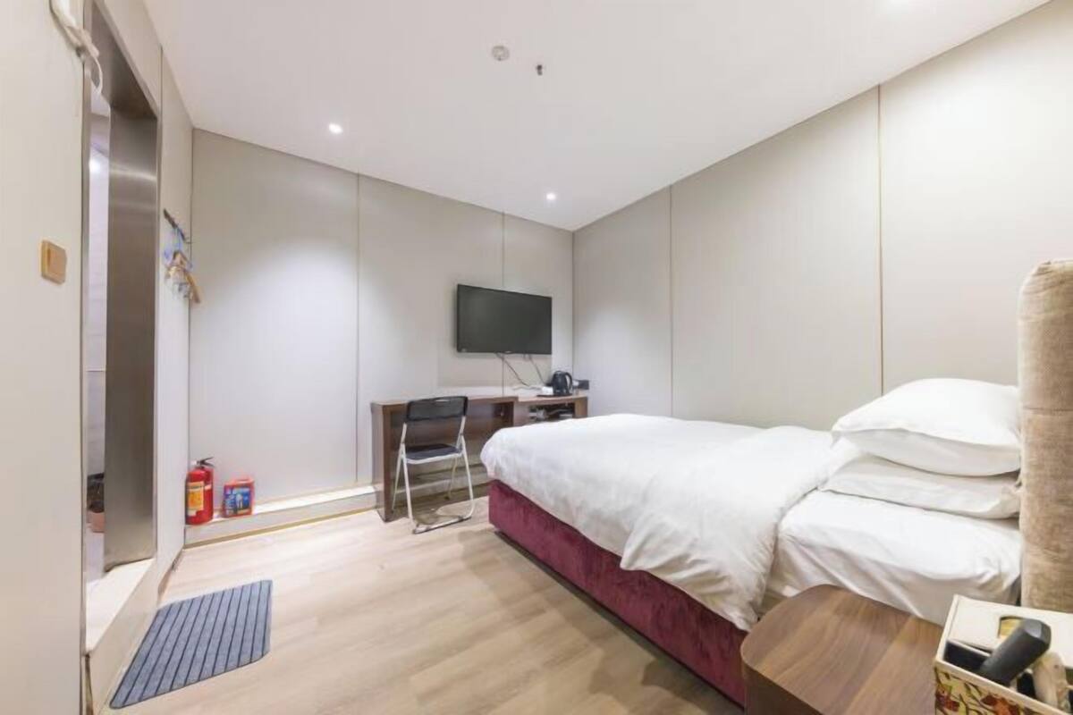 A hotel room with a bed, a desk, a chair, a television, and a fire extinguisher.