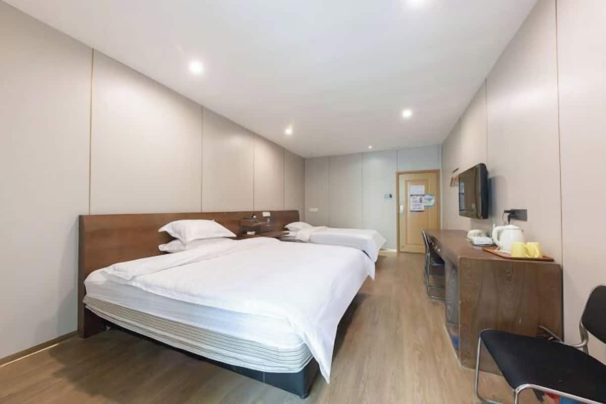 A hotel room with a large bed, a desk with a chair, a television, and a small kitchenette area.