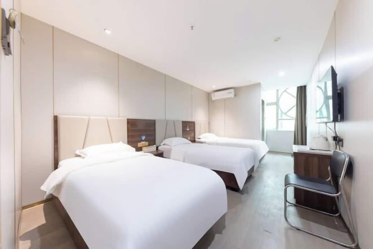 A hotel room with two beds, a desk, a chair, and a TV.