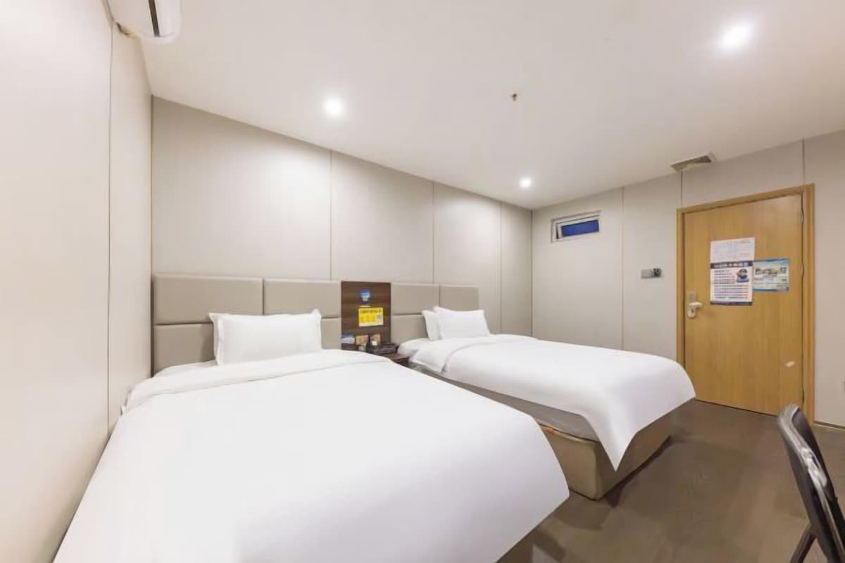 Habitación de hotel con dos camas, una puerta de madera y una mesita con lámpara.