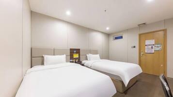 A hotel room with two beds, a wooden door, and a small table with a lamp.