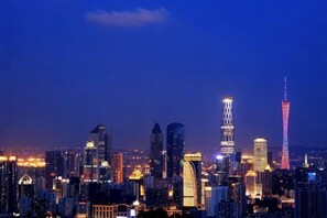 A city skyline at dusk with illuminated buildings and a prominent tower. - Baiyuan Hotel (Baogang Avenue Subway Station) (Guangzhou)