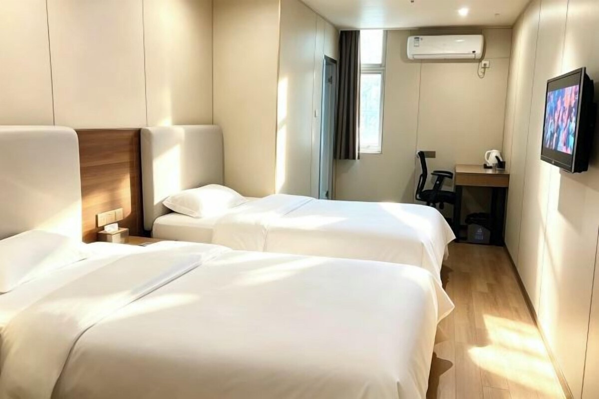 Quarto de hotel com duas camas, uma escrivaninha, uma cadeira, ar condicionado e uma televisão.