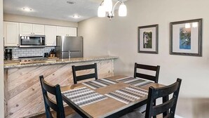 Eine moderne Küche mit weißen Schränken, einer Granit-Arbeitsplatte, einem Edelstahl-Kühlschrank und einem Essbereich mit Holztisch und -stühlen.