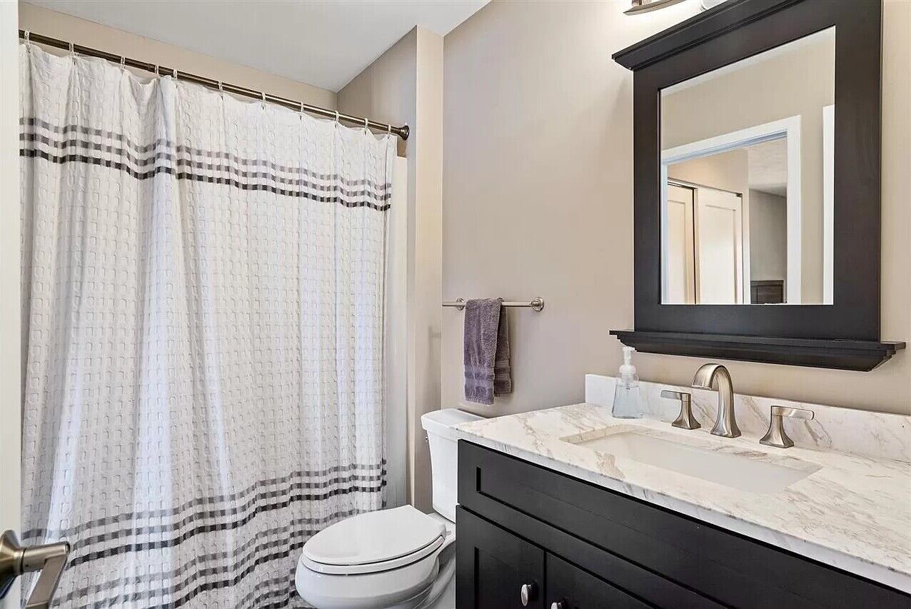 A bathroom with a white toilet, a black vanity with a marble countertop, a large mirror, and a shower curtain with a checkered pattern.