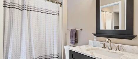 A bathroom with a white toilet, a black vanity with a marble countertop, a large mirror, and a shower curtain with a checkered pattern.