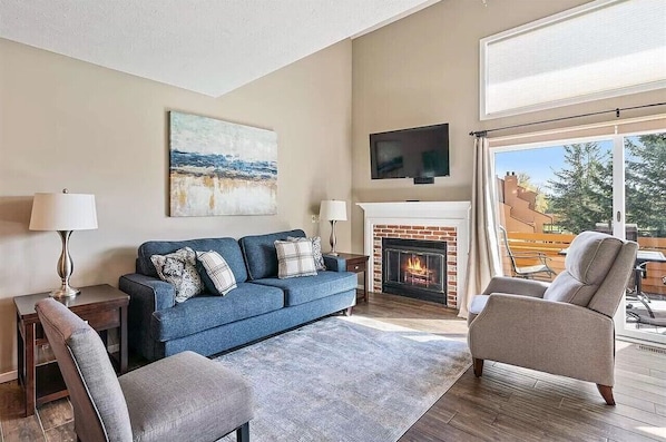 Una sala de estar con un sofá azul, dos sillones, una chimenea y un televisor montado en la pared.