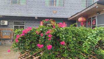 Un edificio con fachada de tejas, cerca de madera con plantas en flor y una unidad de aire acondicionado visible.
