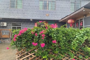 Un edificio con fachada de tejas, cerca de madera con plantas en flor y una unidad de aire acondicionado visible.