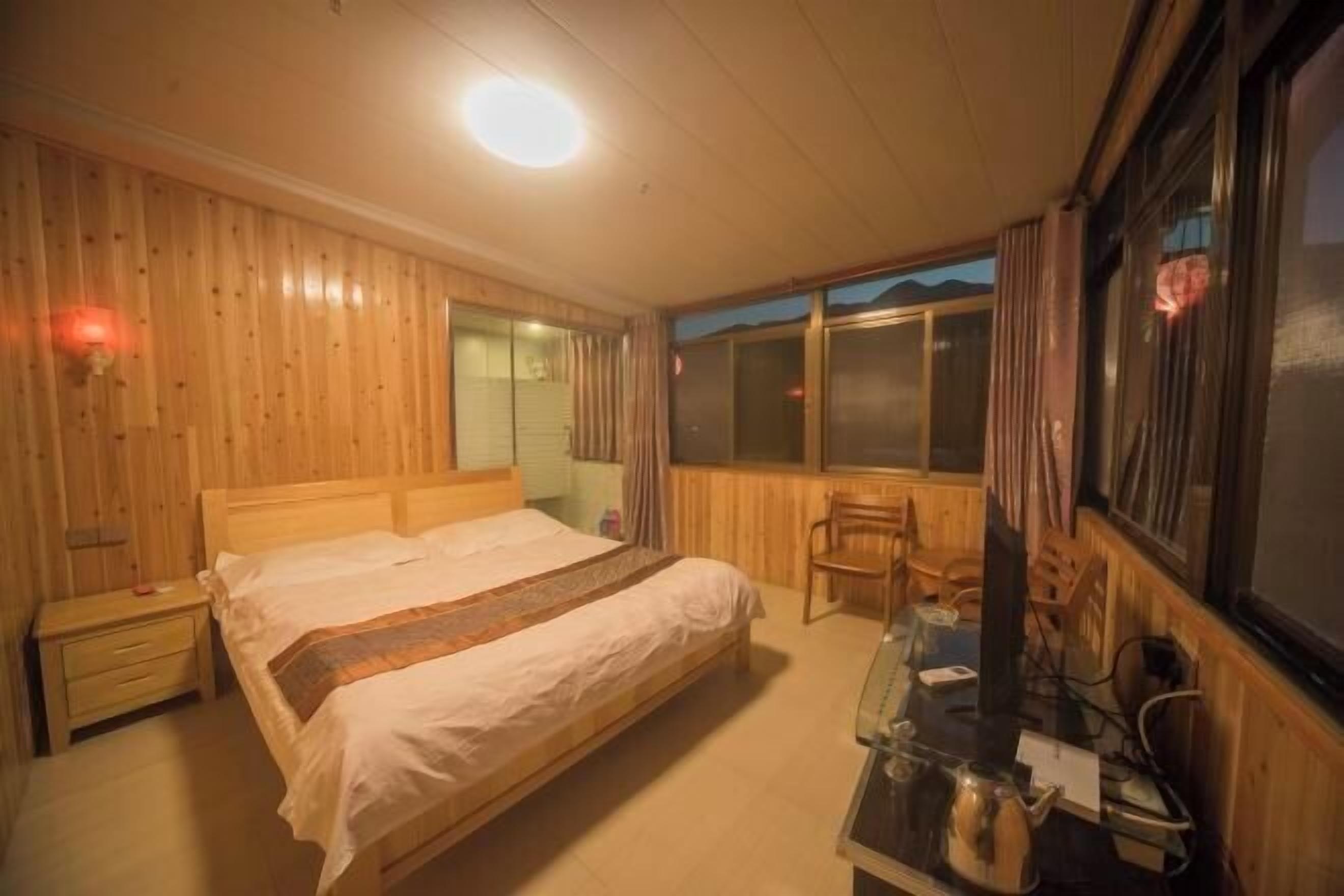 A wooden-paneled bedroom with a bed, bedside table, chair, and a window with a view.