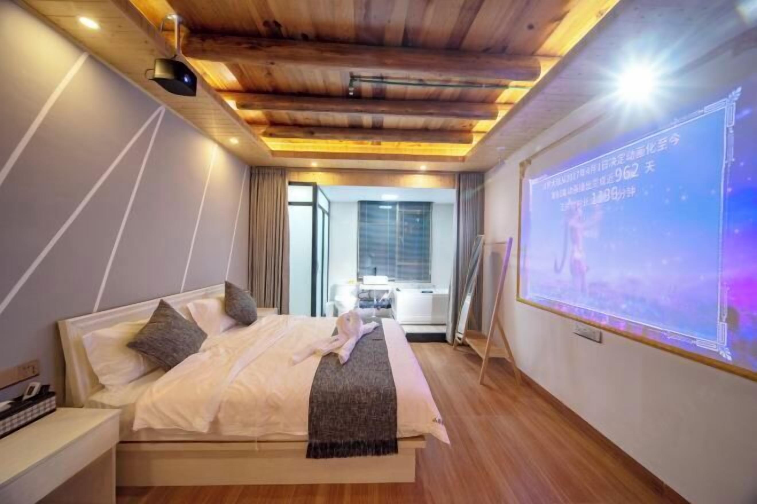 A modern hotel room with a wooden ceiling, a bed with pillows, a nightstand, and a projection screen on the wall.