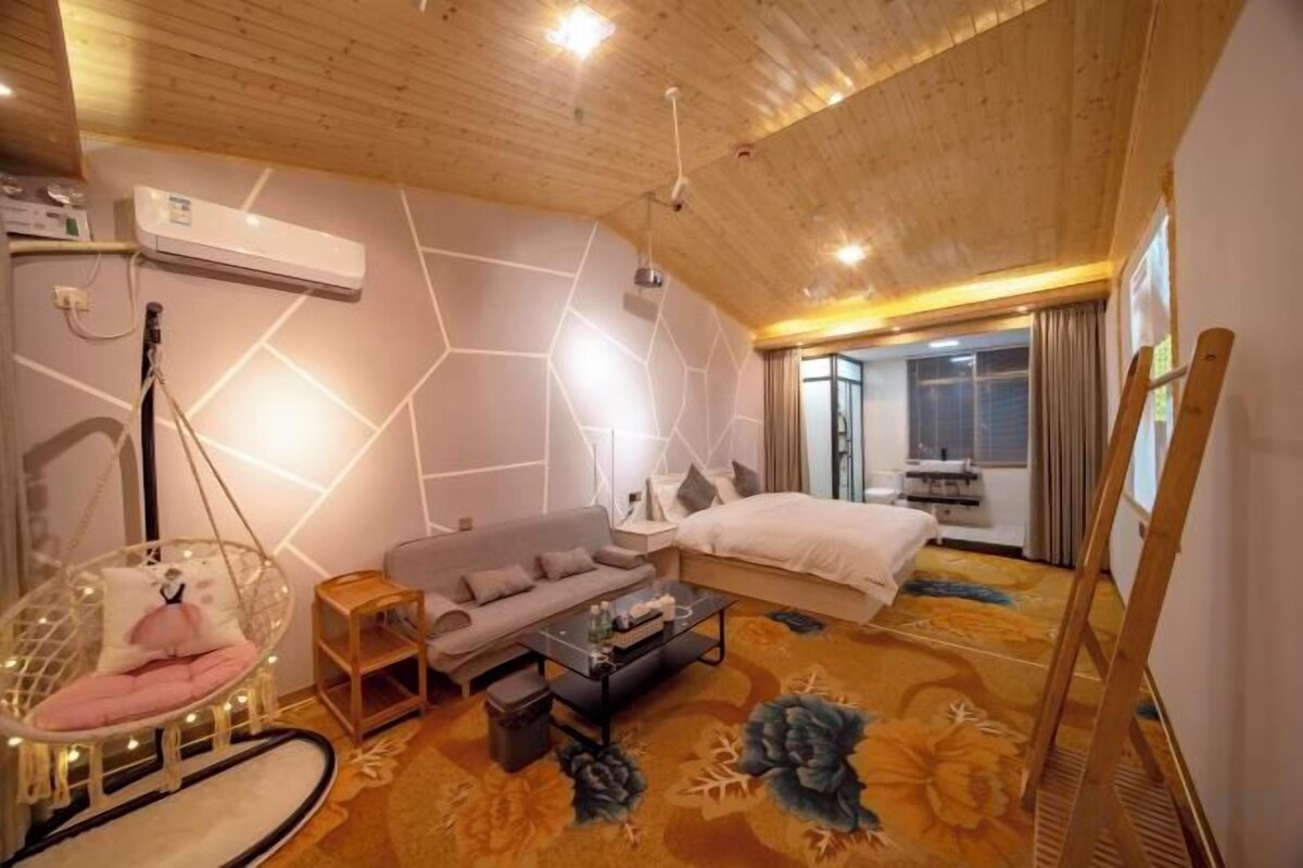A modern hotel room with a wooden ceiling, a bed, a sofa, a hanging chair, and a large window.