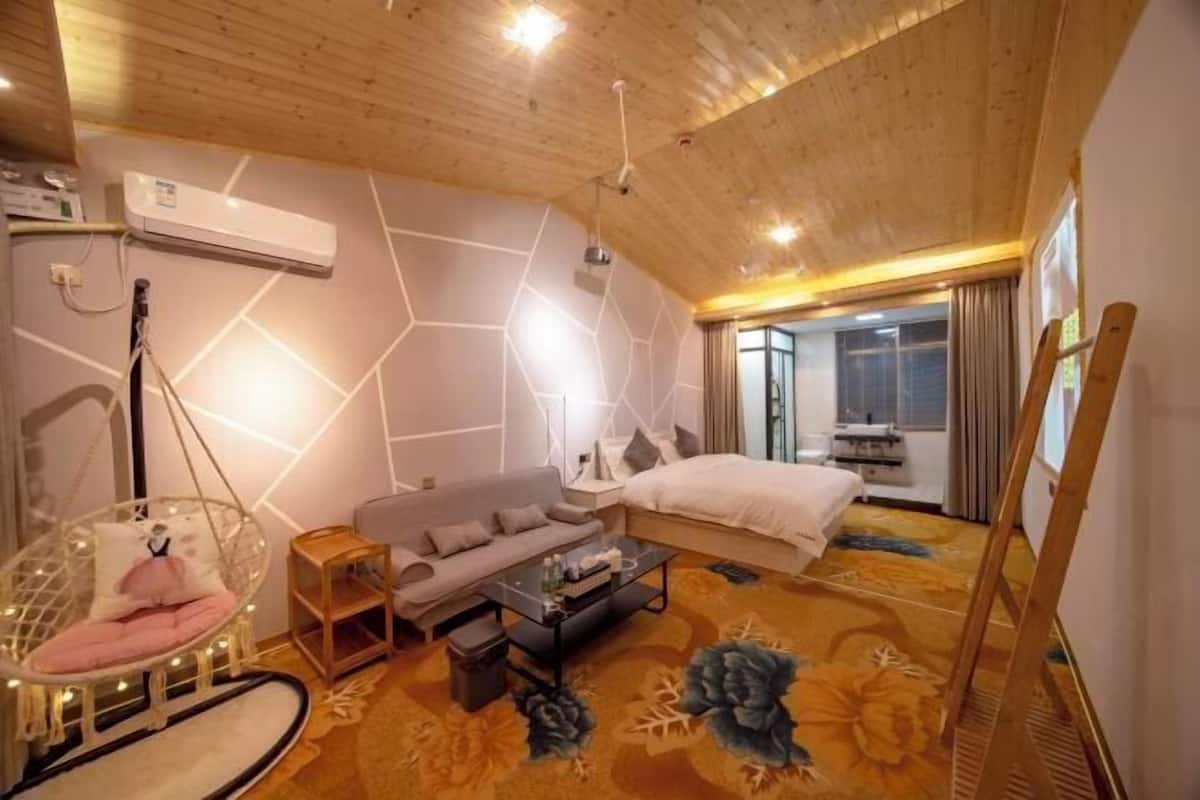 A modern hotel room with a wooden ceiling, a sofa, a bed, a hanging chair, and a large window.