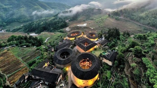 Un ensemble de bâtiments traditionnels à toits arrondis, situés dans un paysage vallonné parsemé de terrasses agricoles.