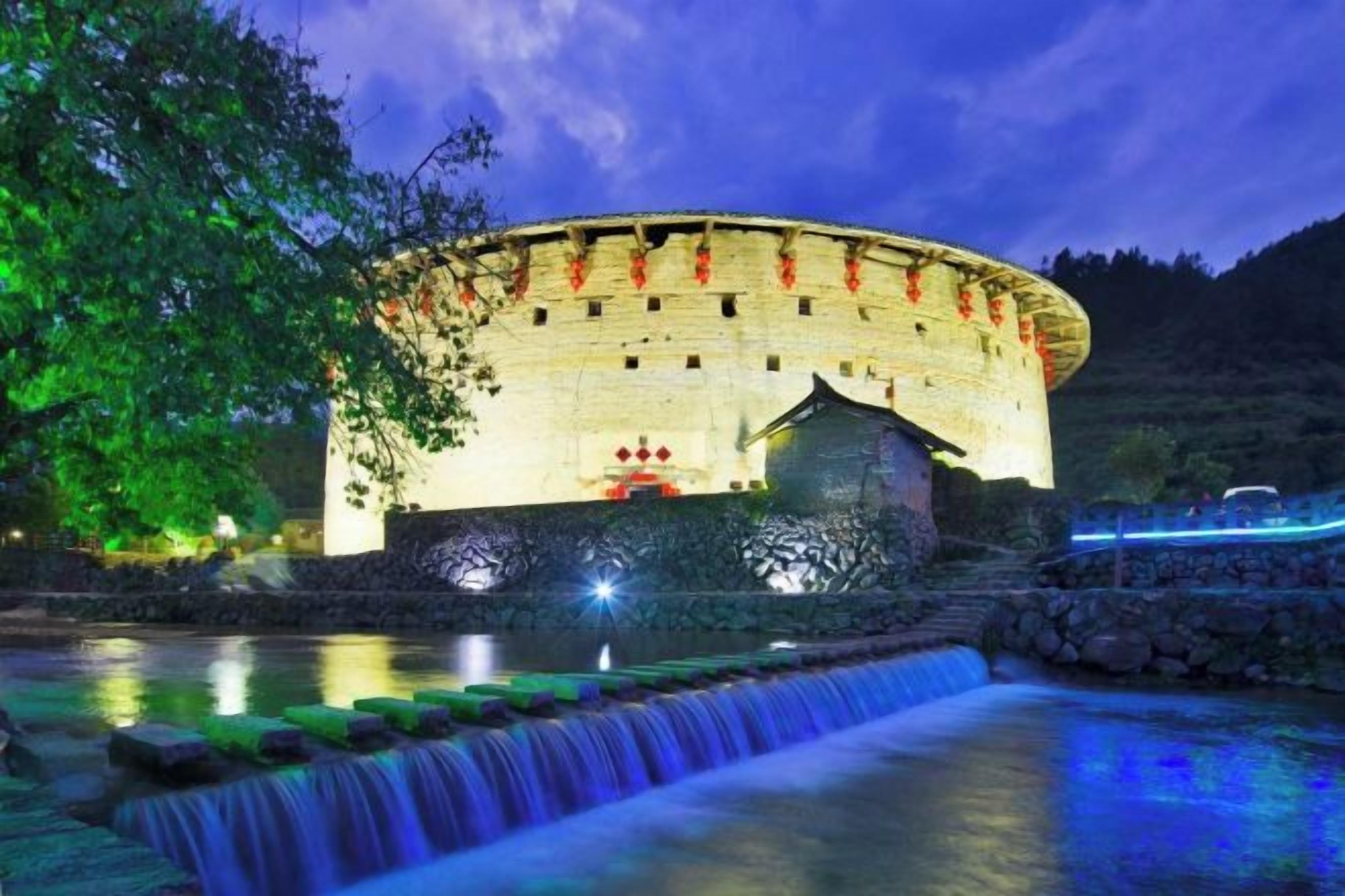 A historic stone building with a circular structure, a small adjacent building, and a water feature in front.