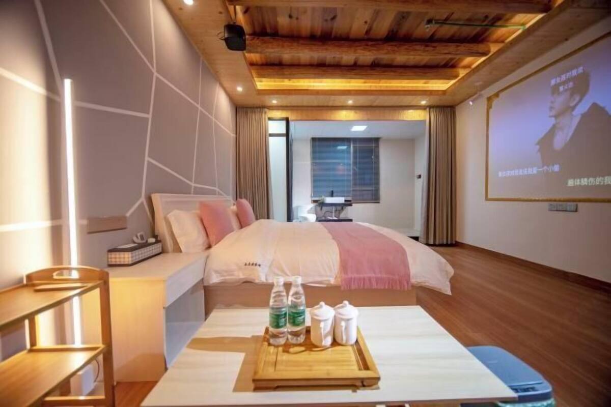 A hotel room with a bed, bedside table, and a projector screen displaying a person.