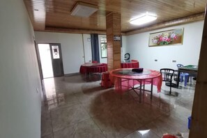 A room with a wooden ceiling, a tiled floor, a round table with chairs, and a door in the background. - Yunshuiyao Brigdehead Inn (Nanjing County)