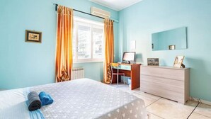A bedroom with a bed, a desk, a chair, a dresser, and a window with curtains.