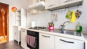 A modern kitchen with white cabinetry, a gas stove, a sink, and various kitchen utensils hanging on the wall.