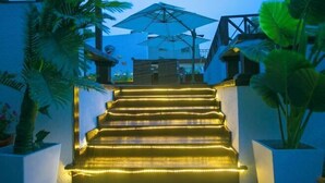 A staircase with illuminated steps leading to a building entrance, surrounded by potted plants and a blue umbrella. - LongXianJu Hotel (Shengsi)