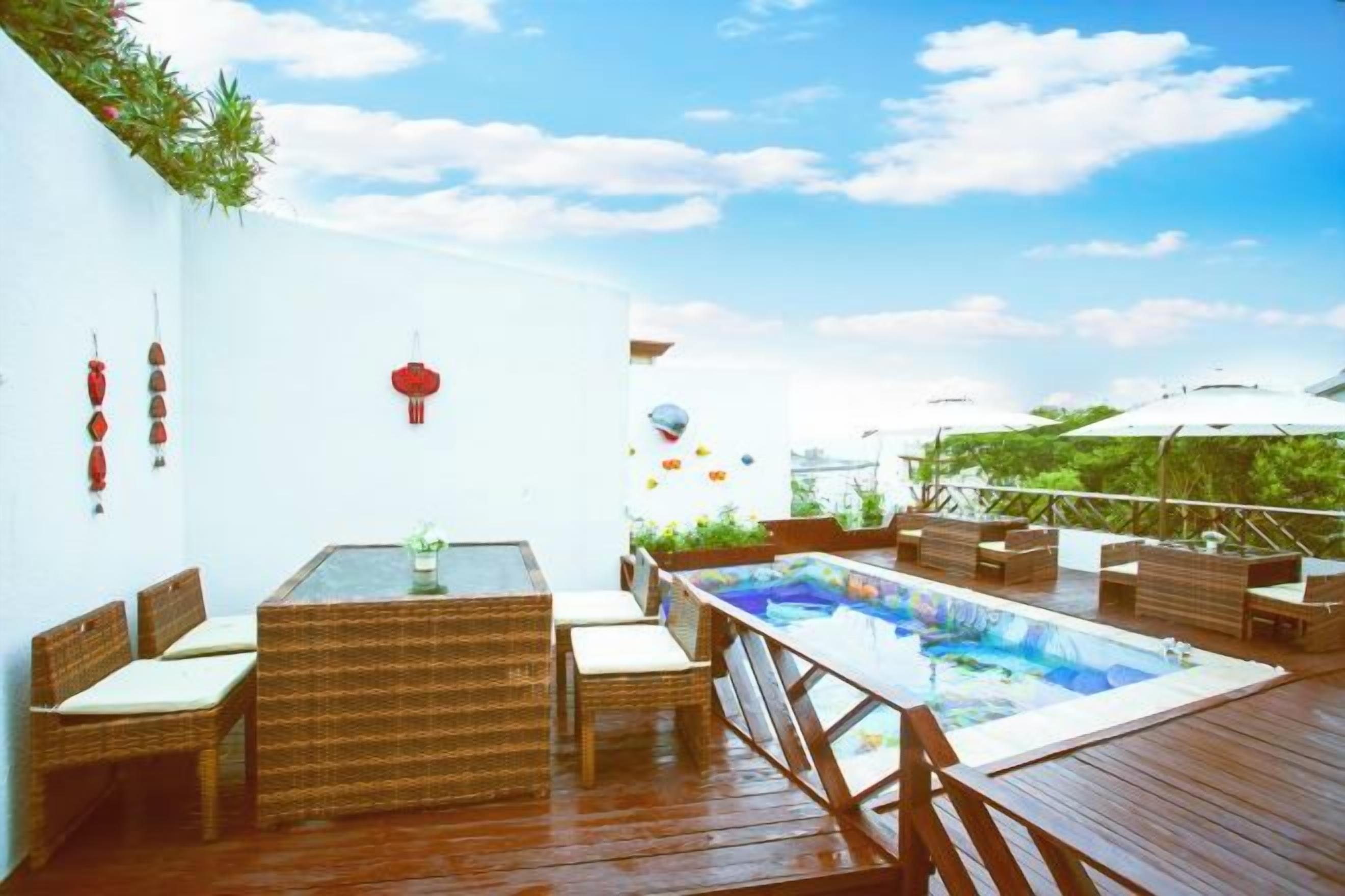 A wooden deck with a pool, wicker furniture, and a white wall with decorations.