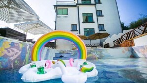 A swimming pool with inflatable swans and a rainbow decoration, surrounded by a tiled deck and a building in the background. - LongXianJu Hotel (Shengsi)