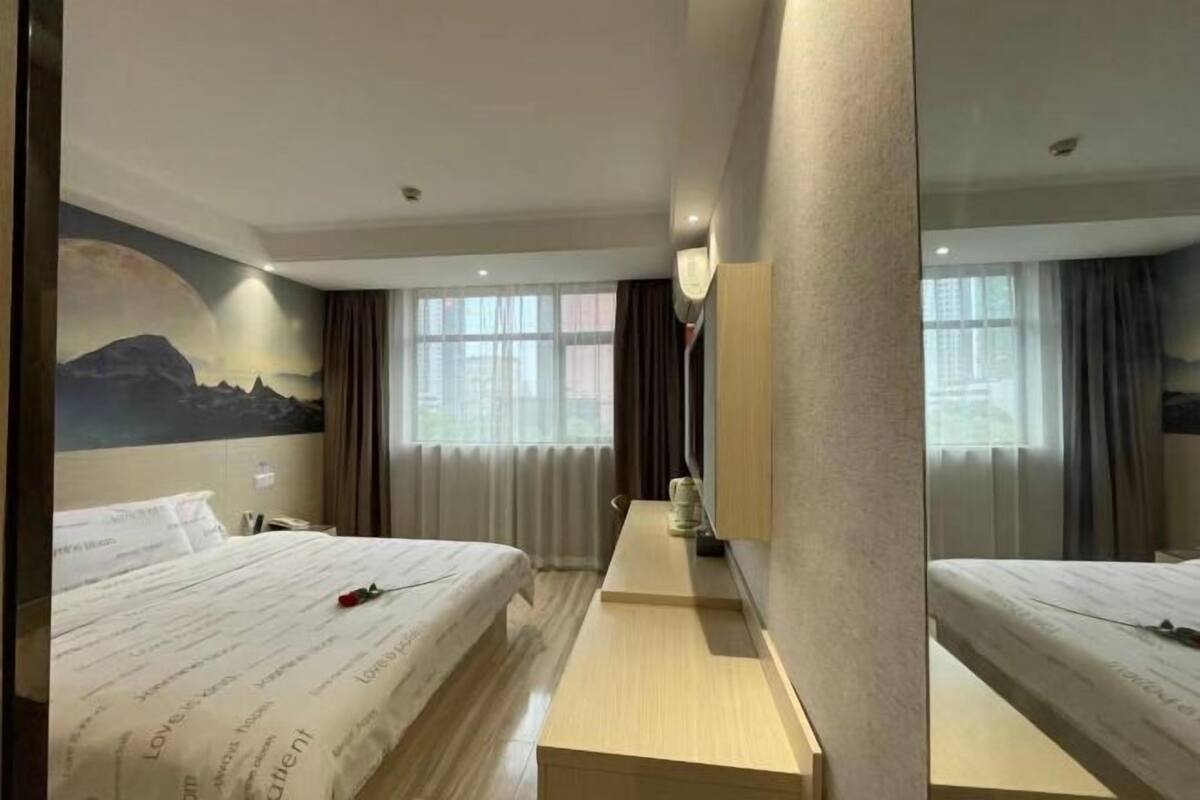 A hotel room with a bed, a desk, a mirror, and a window with curtains.