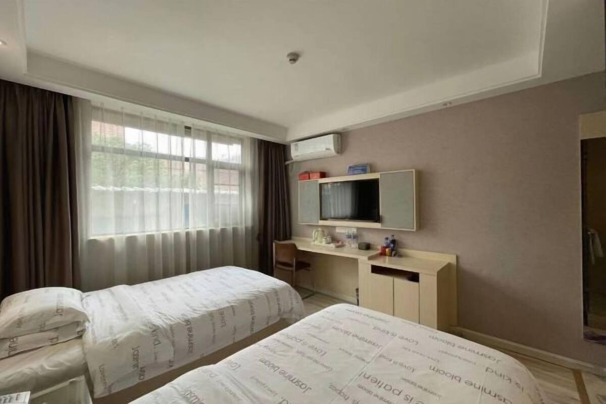 A hotel room with two beds, a desk, a TV, and a shower area.