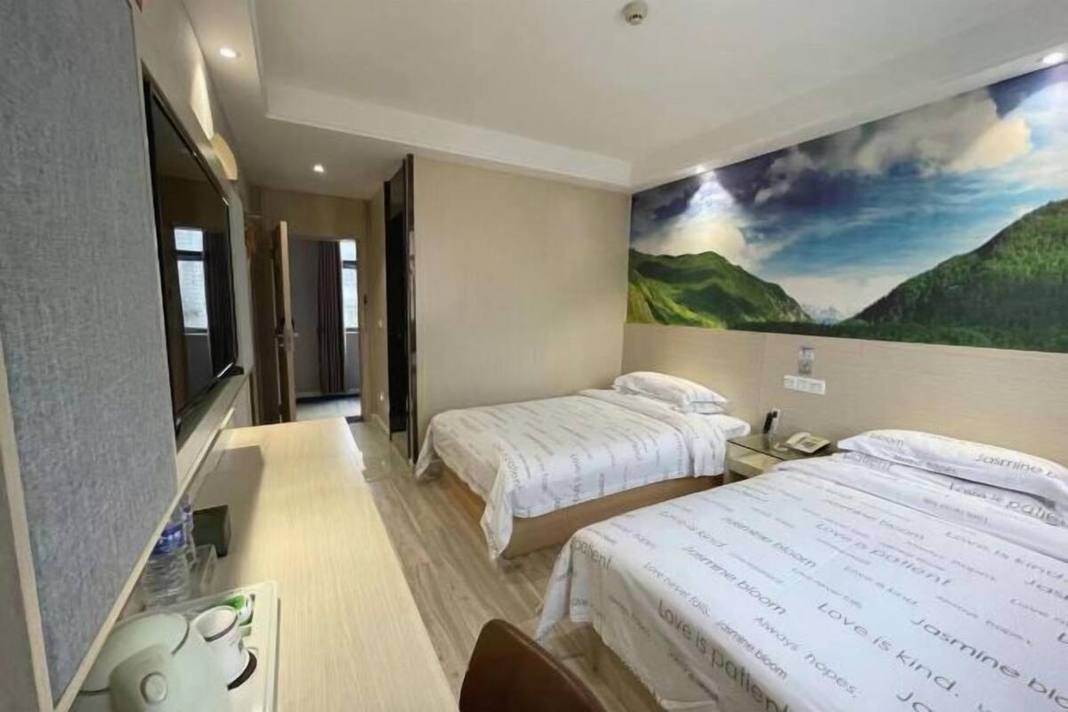 A hotel room with two beds, a desk, a chair, a TV, and a painting of a landscape.