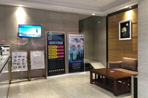 Un área de recepción con mostrador, un televisor en la pared y dos grandes carteles informativos.