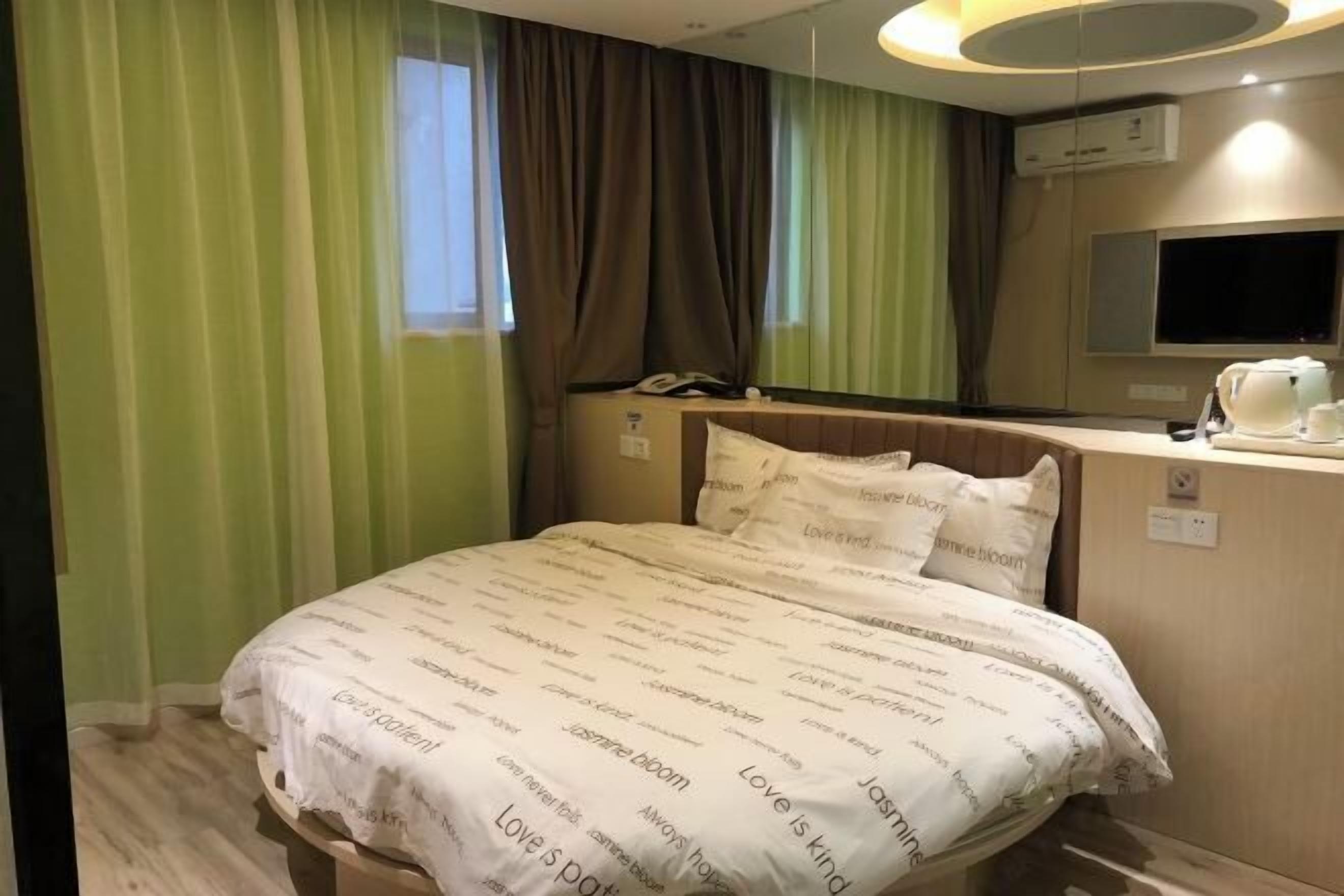 Quarto de hotel com cama, cortinas, mesa de cabeceira com telefone, televisão e máquina de café.