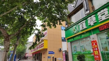 Une vue de rue avec une devanture de magasin verte, un bâtiment jaune et un trottoir bordé d’arbres.