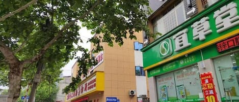 Vista de la calle con un escaparate verde, un edificio amarillo y una acera arbolada.