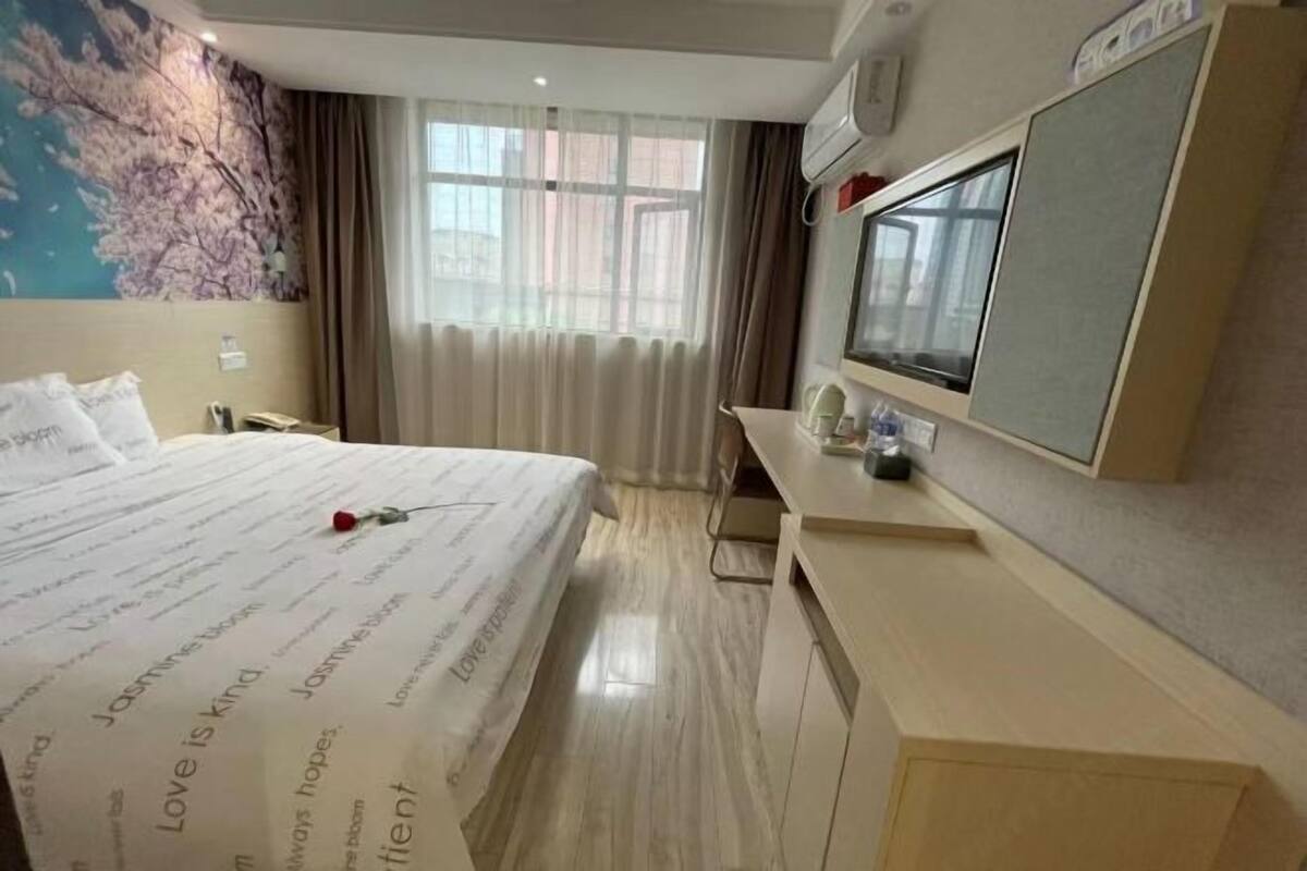 A hotel room with a bed, a desk, a TV, and a window with curtains.