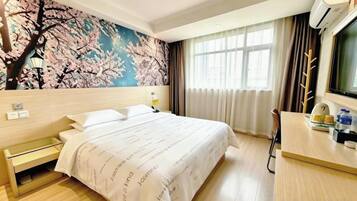 Habitación de hotel con cama, escritorio, silla, ventana con cortinas y un mural de flores de cerezo en la pared.