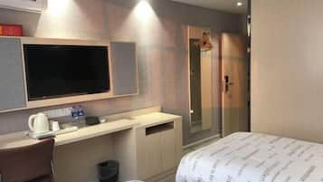 Quarto de hotel com cama, secretária, televisão, chuveiro e guarda-roupa.