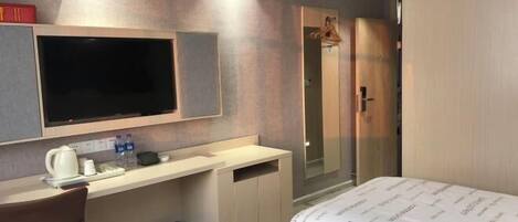 A hotel room with a bed, a desk, a TV, a shower, and a wardrobe.