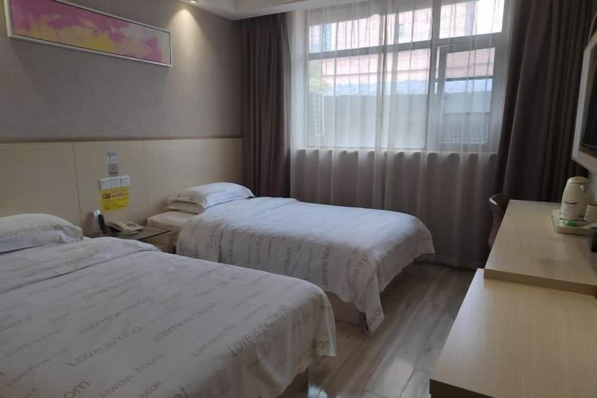 A hotel room with two beds, a desk, a window with curtains, and a wall-mounted phone.