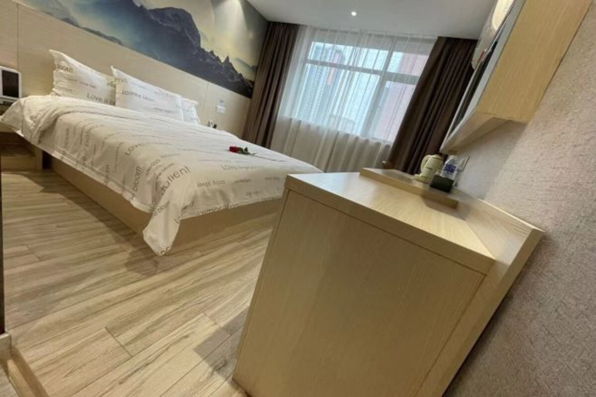 Habitación de hotel con cama, escritorio de madera, televisor montado en la pared y ventana con cortinas.
